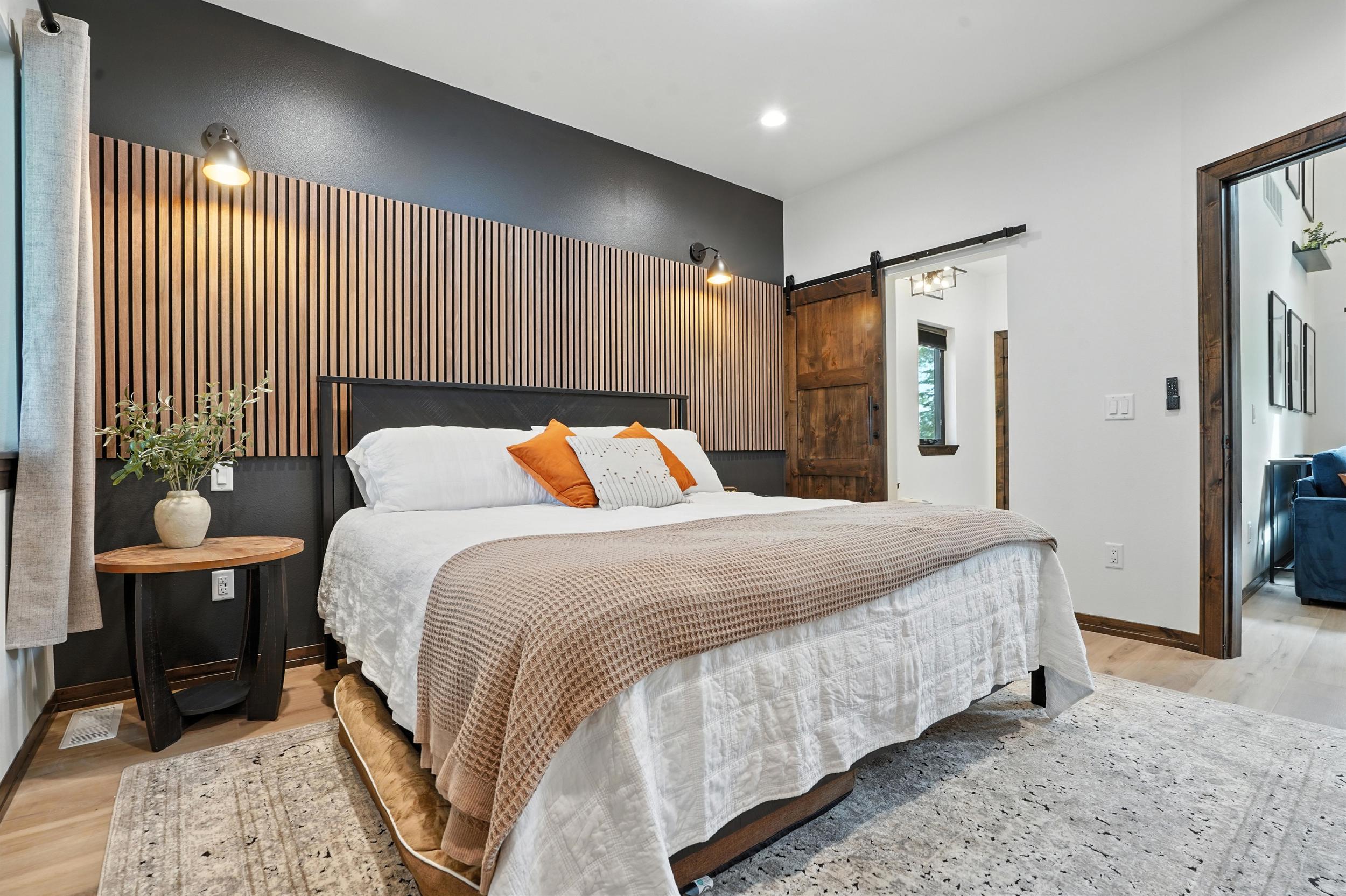 A bedroom with a wood-slat accent wall, a sliding barn door and a white bed with orange pillows